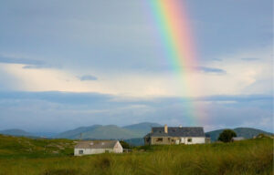 Irland beste Reisezeit mit Regenbogen über grünen Feldern und Wolken am Himmel.