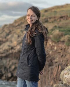 Nahaufnahme von Nadja Uebach, die bei Sonnenuntergang an der Küste von Irland steht.